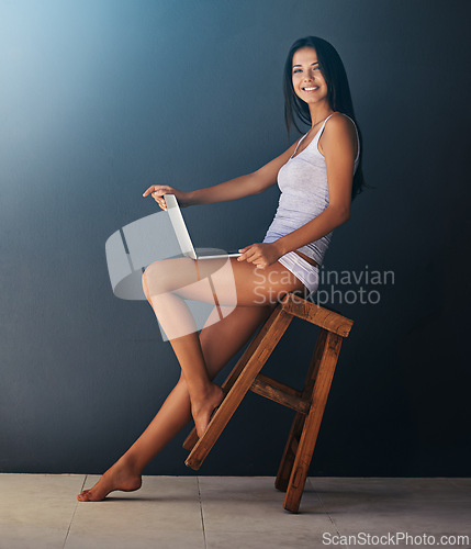Image of Laptop, portrait and woman on chair in studio with gray wall background for social media. Computer, relax and underwear with happy young person leaning or rocking on stool for blogging or streaming