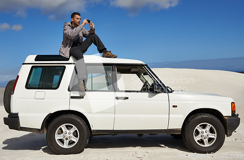 Image of Road trip, man and sitting on car with cellphone and photography for holiday or driving adventure in nature. Guy, memory or social media on vacation by blue sky, sport or rugged terrain for vehicle