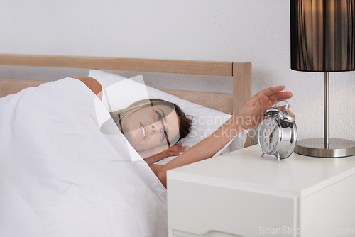 Image of Woman, bed and alarm in bedroom for upset, tired and sleepy for morning, awake and annoyed at home. Young person and moody with clock on bedside table for time and hour for late with blanket