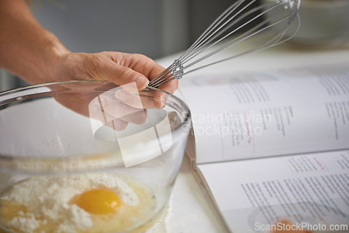 Image of Hands, person and whisk with bowl, kitchen and cookbook for baking. Baker, muffin or food with countertop, eggs and flour for recipe preparation and recreation or hobby at home or house with utensils