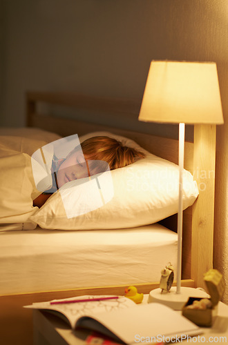 Image of Boy, bedroom and rest for night, sleeping and tired with fatigue and peace. Child, dreaming and exhausted with pyjamas, carefree and bed with lamp for serene childhood at home or house for calm kid