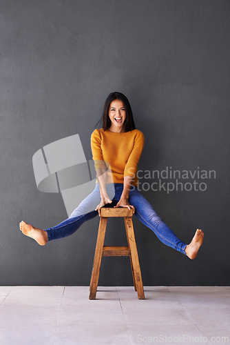 Image of Portrait, fashion and woman on chair in studio for excited, trendy or casual clothing with gray background. Happiness, cheerful and face of person on stool for wardrobe, sweater and stylish outfit