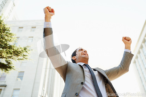 Image of Smile, success and hands raised with businessman in city for celebration of bonus or promotion. Corporate, building and sky with happy employee cheering outdoor in urban town for target or goals