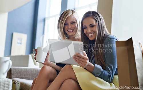 Image of Women, smile and coffee with tablet on sofa for social media, website or internet search in living room. Female people, happy and technology on couch for communication, bonding and recreation at home