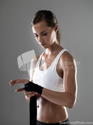 Image of Woman, fitness and boxer with strapping fists for fight, workout or exercise on a gray studio background. Female person or fighter wrapping hands in preparation or getting ready for sports training