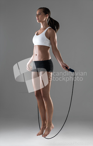 Image of Woman, fitness and jumping with rope in cardio workout, exercise or training on a gray studio background. Active female person or athlete skipping in balance, challenge or weight loss on mockup space