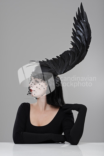 Image of Fashion, woman and hat with feather in studio for glamour, style and thinking with mystery. Female person, confidence and cap with wing for elegance, luxury and designer clothes on gray background