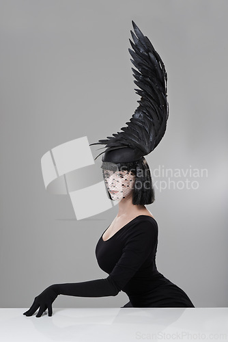 Image of Accessory, feather and woman in studio with fashion for glamour, elegance and thinking by table. Female person, designer clothes and cap with wing for chic, style and luxury on gray background