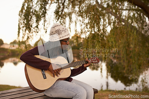 Image of Young woman, playing and guitar on bench by lake for music, passion and talent on string instrument. African lady, musician and composer of song in nature and jazz artist with practice for concert