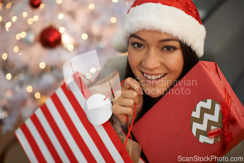 Image of Christmas gift, happy woman and portrait in home with bag for celebration of holiday or festive season in living room. Xmas, face and smile of person with present, hat and bokeh in apartment in Spain