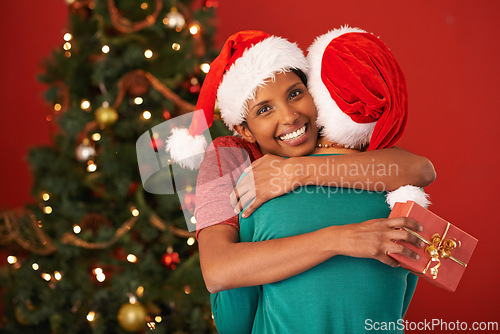 Image of Women, hug and Christmas with surprise, gift box and package on red studio background. Face, people or friends with Xmas present or parcel with embrace or excited with celebration or bonding together