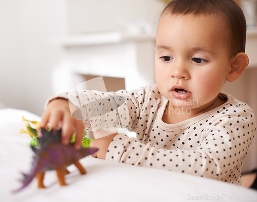 Image of Kid, toddler and play with toy in home, games and dinosaur for child development in bedroom. Person, girl and entertainment for enjoyment in childhood, curious and plastic animal for fun on bed