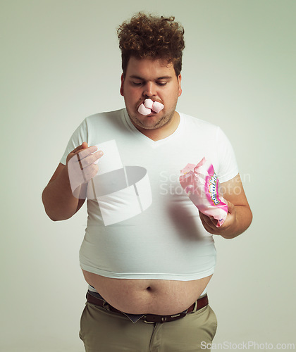 Image of Obesity, weight gain and humor for man in studio with marshmallow for unhealthy eating, sugar and candy. Overweight person with sweets in mouth and fat stomach for greed, comedy and funny indoor