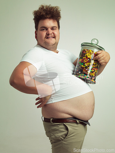 Image of Candy, jar and portrait of man in studio for luxury snacks, sweets and dessert in container. Comic, funny and food, isolated and plus size person with glass for unhealthy diet on background.