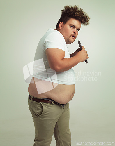 Image of Chocolate, portrait and plus size man with eating food, dessert and candy in a studio. Nutrition, sweet and unhealthy snack with sneaky and secret with a hungry male person with green background