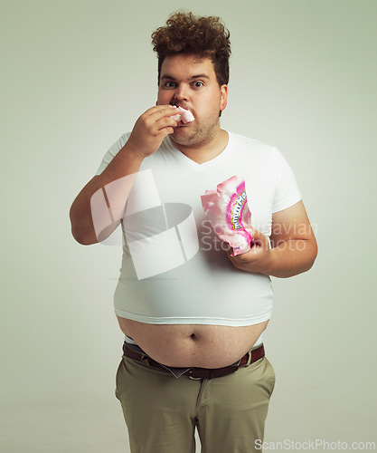 Image of Plus size, candy and portrait for man in studio with marshmallow for unhealthy eating, sugar and confection. Young person with sweets in mouth and round stomach for greed, comedy and humor indoor