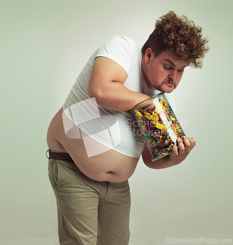 Image of Candy, sweets jar and man in studio for eating snacks, junk food and dessert in container. Comic, funny and isolated and plus size crazy person with glass for unhealthy diet and sugar on background