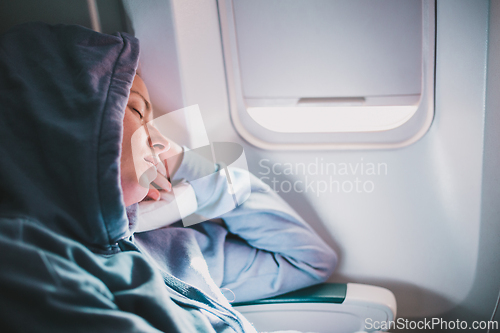 Image of Tired blonde casual caucasian woman wearing sporty hoodie napping on seat while traveling by airplane. Commercial transportation by planes. Authentic image of real people.