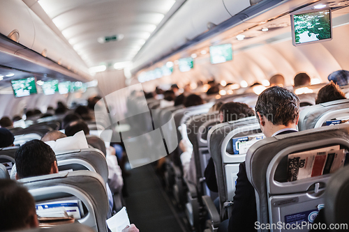 Image of Interior of airplane with passengers on seats and stewardess in uniform walking the aisle, serving people. Commercial economy flight service concept.