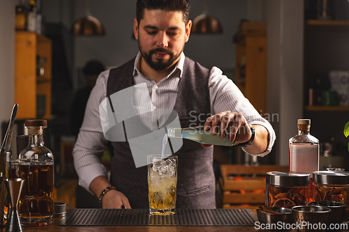 Image of Professional bartender pours cocktail at bar