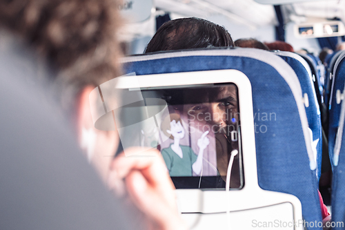 Image of Reflection of a passenger on an airplane touch screen monitor while watching cartoon during long flight. Entertainment service system in aircraft.