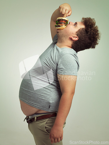 Image of Fast food, hungry and man with hamburger in studio background with lunch, snack and craving for plus size guy. Male person, burger and takeaway for meal in mouth for eating, starving and bite