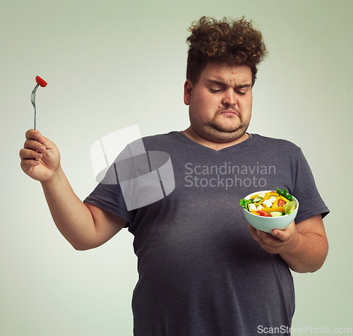 Image of Studio, unhappy man and salad with bowl for healthy meal, diet and nutrition for weight loss. Plus size, male person and disgust expression with organic food for wellness, detox or lifestyle change