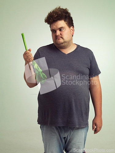 Image of Plus size, diet and unhappy man with vegetable for health, nutrition and wellness in studio in white background. Weight loss, celery and frustrated male person for healthy food, wellbeing and detox