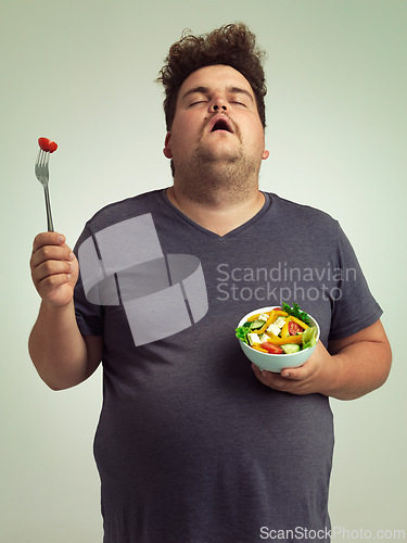 Image of Plus size man, salad and diet with healthy food with fork, bowl and vegetables for wellness on studio background. Male person, frustrated and lose weight for health, eating disorder and nutrition