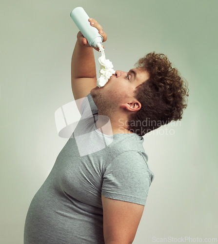 Image of Plus size, eating and man with cream in studio for unhealthy, sugar and sweet snack or dessert. Messy, greedy and hungry male person enjoying whipped dairy product for humor by gray background.