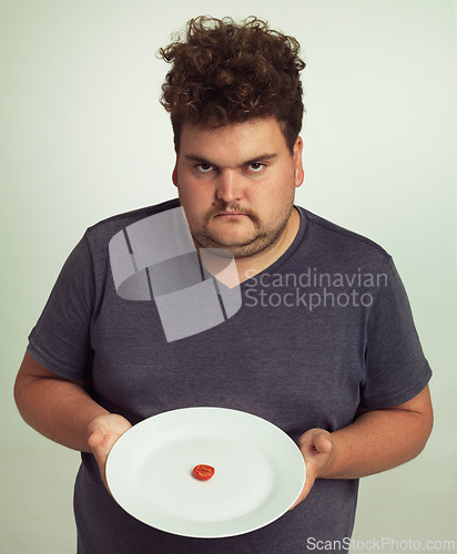 Image of Portrait, diet or plate and plus size man in studio on gray background, unhappy with size of meal. Food, health or nutrition and disappointed young person frustrated with tiny tomato slice serving