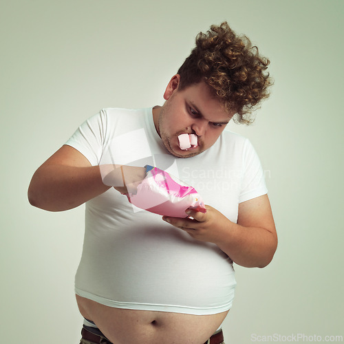Image of Food, hunger and marshmallow with plus size man in studio on gray background for unhealthy eating. Belly, hungry for sweets and candy with young person with snack bag or packet for greed or gluttony