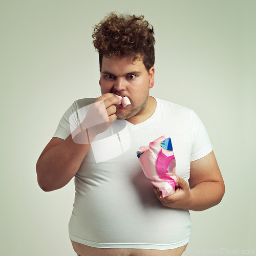 Image of Food, hungry and marshmallow with plus size man in studio on gray background for unhealthy eating. Hunger, appetite for sweets and ravenous young person with snack bag or packet for greed or gluttony