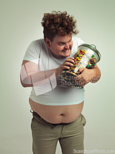 Image of Candy, crazy and plus size man on a white background for snacks, sweets and dessert in container. Comic, funny and isolated overweight person with glass jar for unhealthy diet or sugar in studio