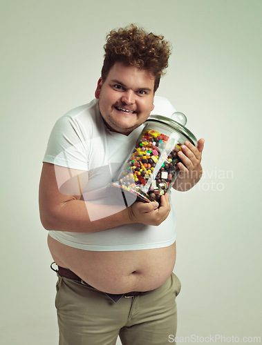Image of Candy, jar and portrait of crazy man in studio for snacks, sweets and dessert in container. Comic, funny and overweight, isolated and plus size person with glass for unhealthy diet on background