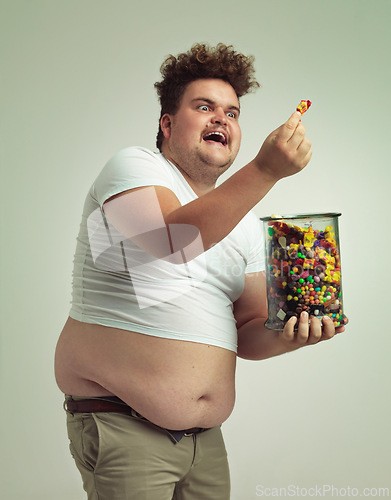 Image of Excited, man and happy with candy in studio for treat, snack and cheerful with unhealthy diet. Plus size, male person and jar of sweets with sugar food for happiness, enjoyment and satisfaction