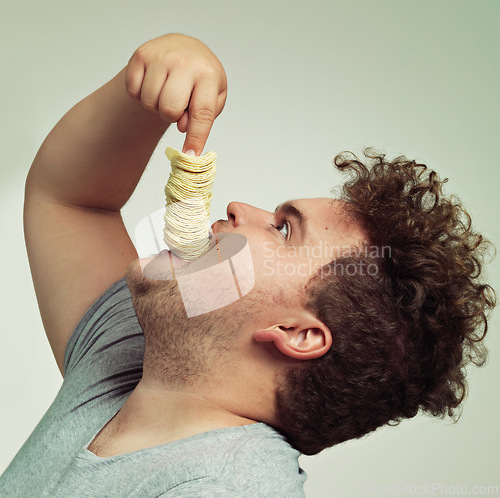 Image of Overweight, eating and man with chips in studio for unhealthy, potato and salty snack. Plus size, food and profile of male person enjoying stack of crisps in mouth isolated by gray background.