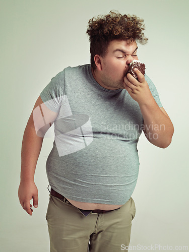 Image of Obesity, eating and man with cake in studio for unhealthy, sugar and sweet snack. Greedy, overweight and plus size person enjoying messy slice of chocolate dessert isolated by gray background