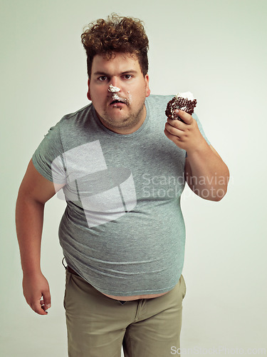 Image of Plus size, eating and portrait of man with cake in studio for unhealthy, sugar and sweet snack. Greedy, food and male person with messy slice of chocolate dessert isolated by gray background.