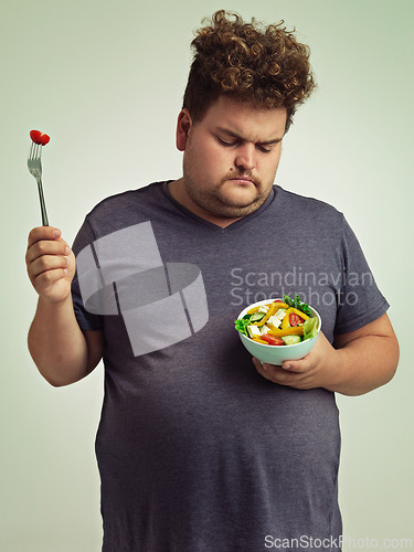 Image of Unhappy, man and salad for diet with healthy food, fork or bowl and vegetables for wellness on studio background. Plus size person, fresh meal and lose weight for health, eating disorder or nutrition