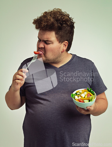 Image of Man, salad and eating with disgust in studio for healthy diet, nutrition and unhappy for weight loss. Plus size, male person and fork with tomato for vitamin c, detox or organic food for lifestyle