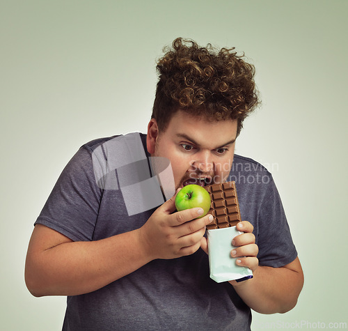 Image of Person, apple and chocolate in studio with choice of junk food, sweet or diet for wellness. Plus size, man eating and decision, fruit or candy for nutrition, lose weight and healthy lifestyle