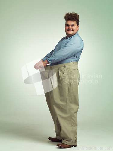 Image of Happy man, plus size and weight loss with pants for measurement or waist on a studio background. Male person with smile for healthy diet, nutrition and oversize in fashion or clothing on mockup space