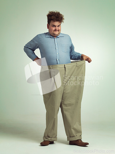 Image of Happy man, portrait and plus size with pants for waist, weight loss or measurement on a studio background. Male person with smile for healthy diet, obesity or overweight clothing on mockup space