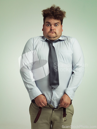 Image of Man, portrait and shocked with plus size pants or big waist in obesity, overweight or measurement on a studio background. Young male person struggling to fit clothing with body fat or chubby stomach