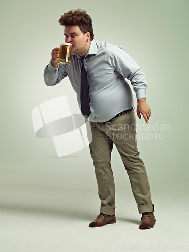 Image of Man, obesity and drinking with beer for alcohol, belly or party on a studio background. Male person or plus size model with keg, glass or mug for beverage, wine or unhealthy drink on mockup space