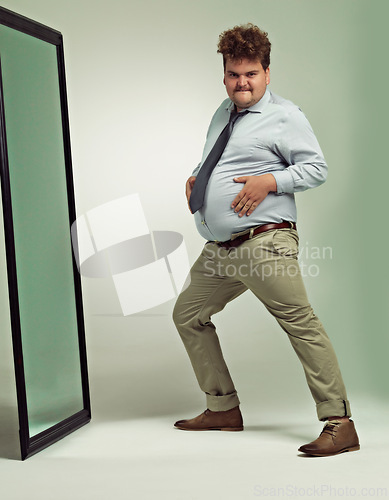 Image of Funny, portrait and man happy with mirror, plus size and overweight with hand on stomach or abdomen. Confident, male person and guy with double chin from fat in body, unique and crazy in studio