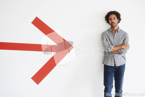 Image of Man, portrait and arms crossed with arrow by wall in car park with confidence, mockup space and travel. African person, face and serious tourist in parking area with direction, sign and symbol