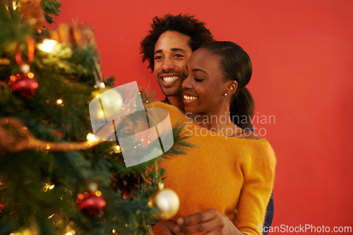 Image of Couple, Christmas and tree decoration in home with happiness for vacation celebration, giving or bonding. Man, woman and smile with lighting for winter season for family event, embrace or lounge