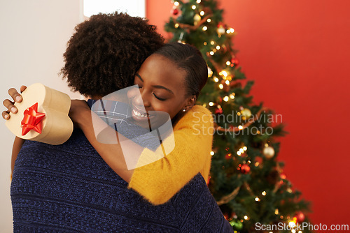 Image of Christmas, present and black couple in hug with box or opening surprise on festive holiday or vacation with happiness. Embrace, woman and man offer a gift in home with love and kindness in marriage